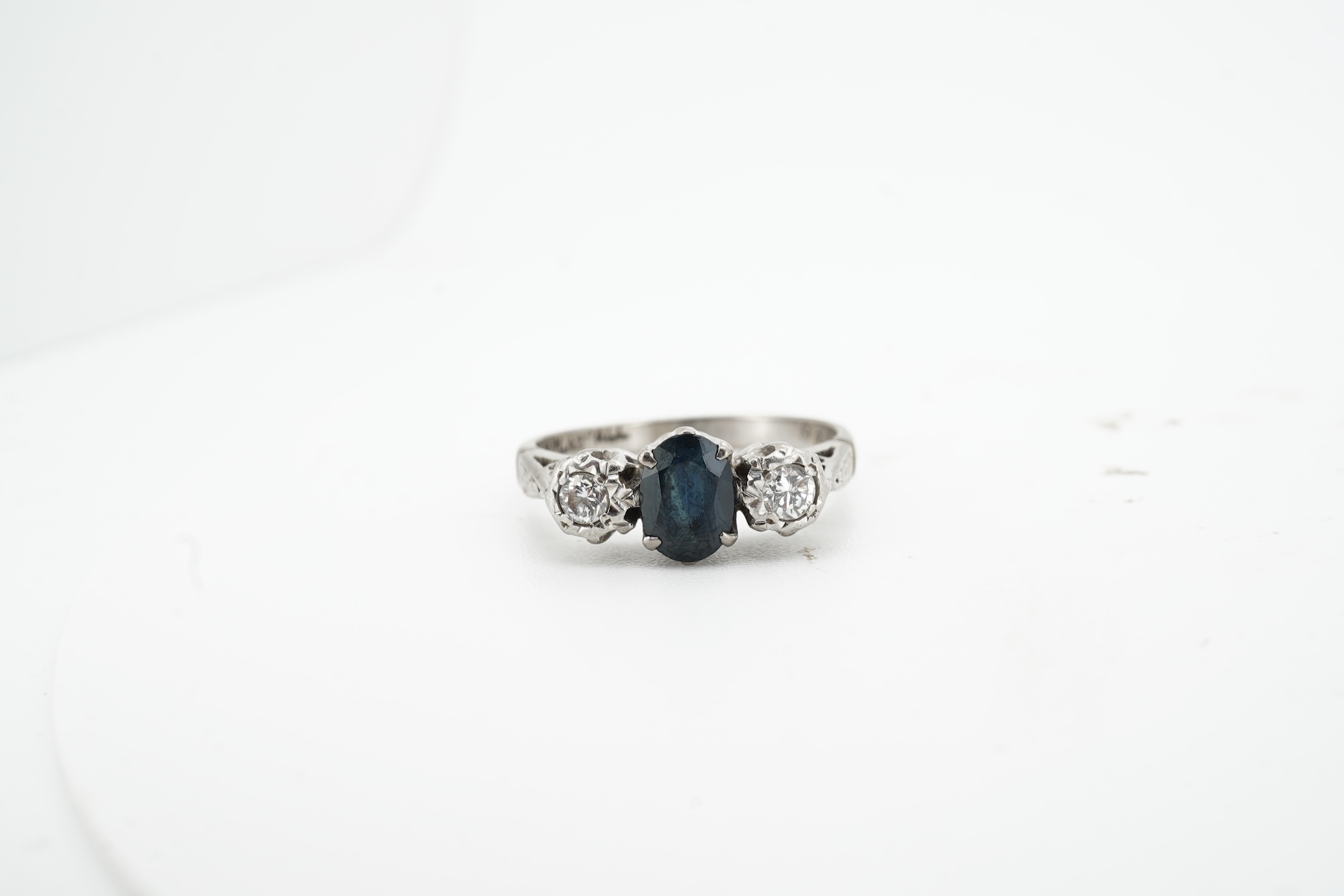 A sapphire and diamond ring, claw-set with an oval sapphire measuring approximately 6.2 x 4.5 x 3.2mm, between shoulders set with brilliant-cut diamonds totalling approximately 0.14 carats, mounted in platinum and pallad